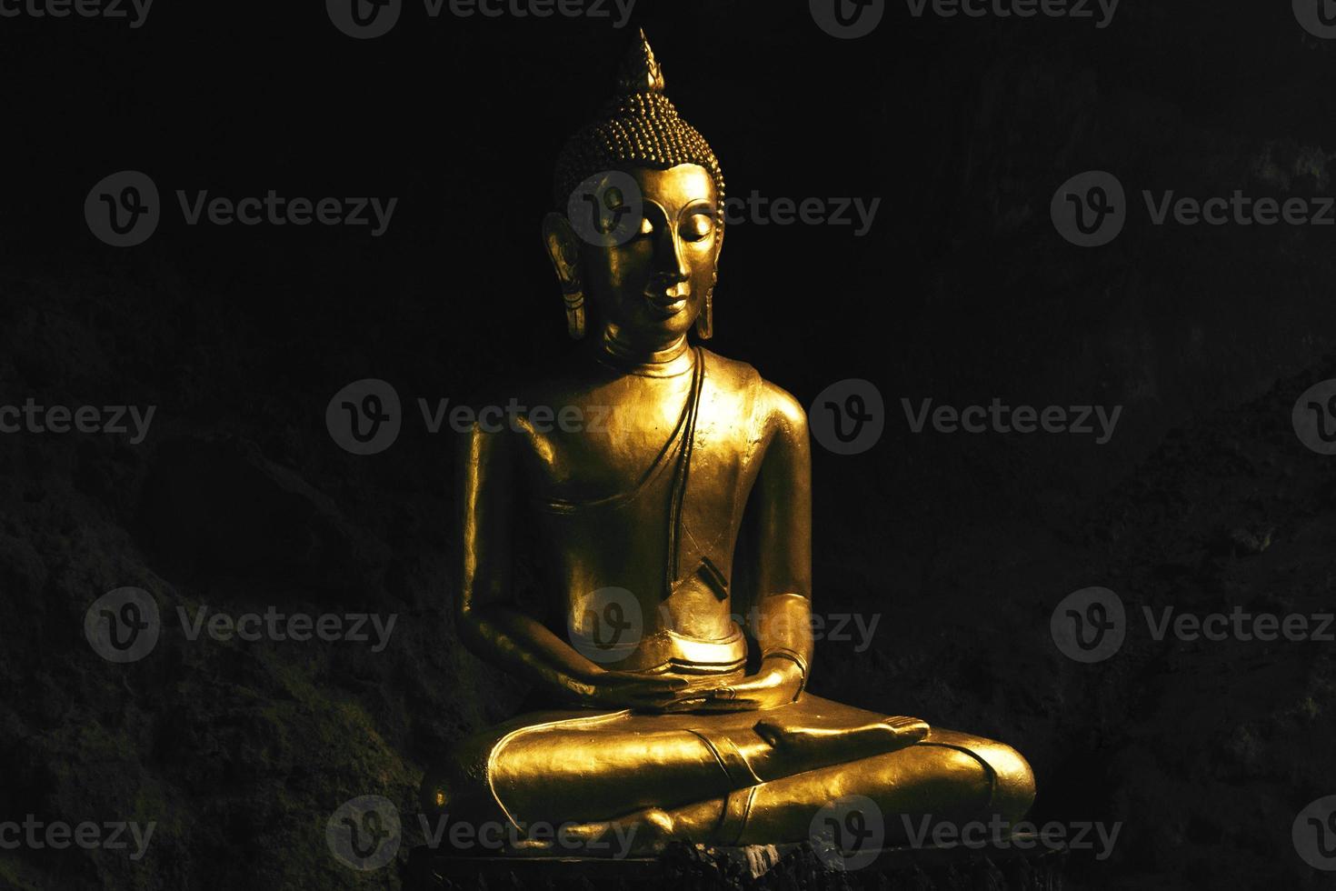 estátua de Buda de bronze rezando em pose de lótus dentro de uma caverna. foto
