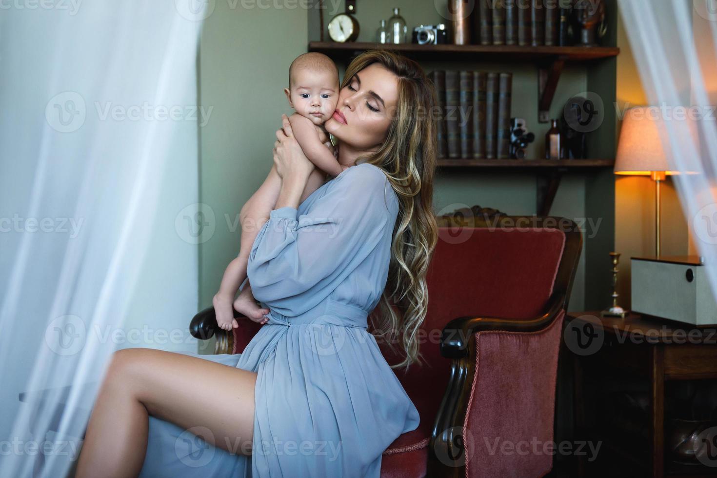 jovem linda mãe usando vestido cinza de luxo segurando seu bebê nas mãos foto