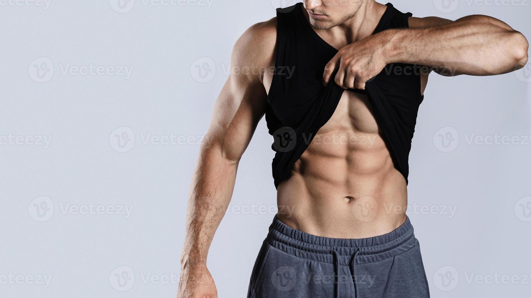 fisiculturista mostrando seus músculos abdominais contra fundo cinza foto