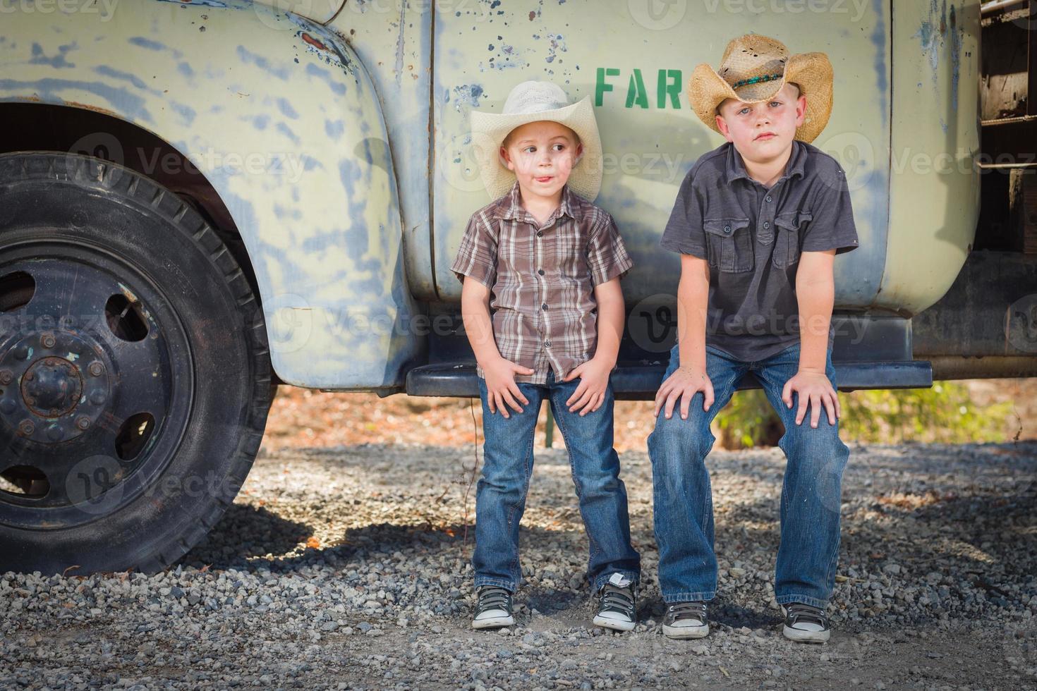 dois meninos usando chapéus de caubói encostados em um caminhão antigo em um ambiente campestre rústico. foto