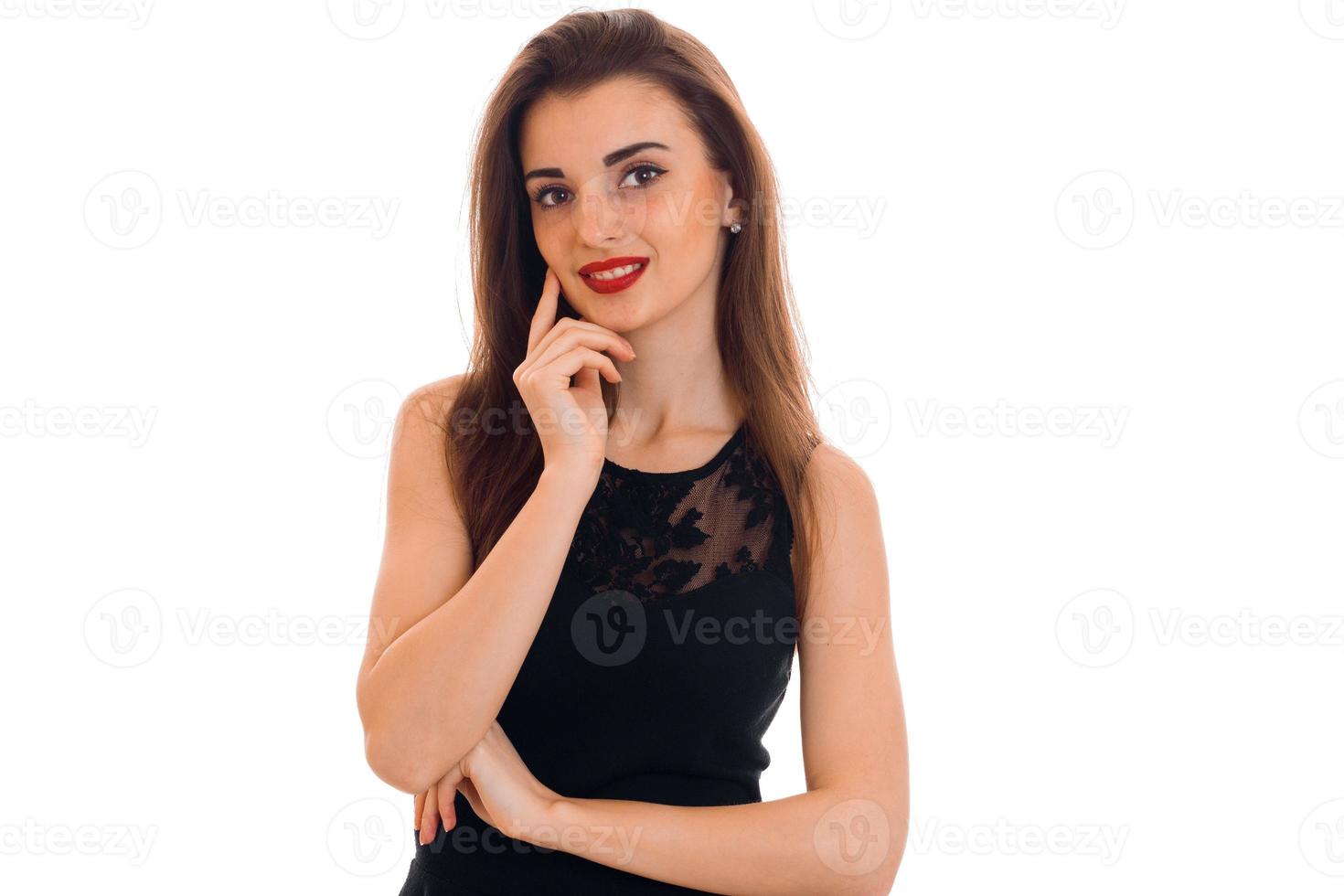 retrato de alegre jovem morena com lábios vermelhos em vestido preto olhando para a câmera e sorrindo isolado no fundo branco foto