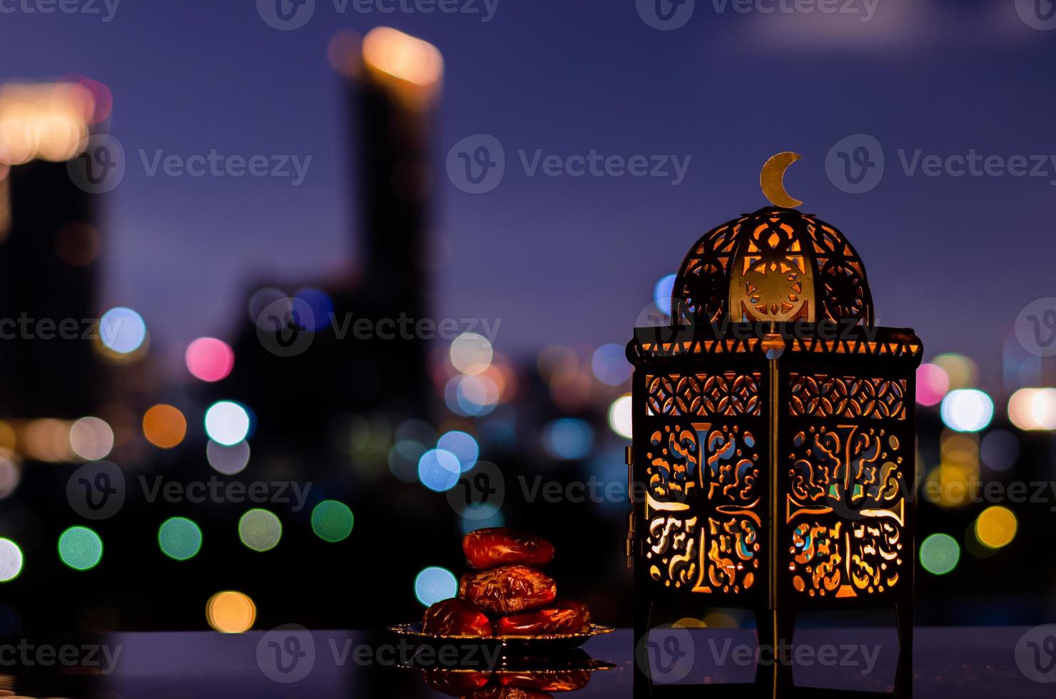 lanterna e pequeno prato de frutas tâmaras com céu noturno e cidade bokeh luz de fundo para a festa muçulmana do mês sagrado do ramadã kareem. foto