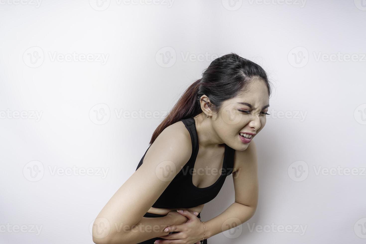 uma jovem doente doente vestindo roupas esportivas segura a mão no estômago sofre dor isolada no fundo branco foto