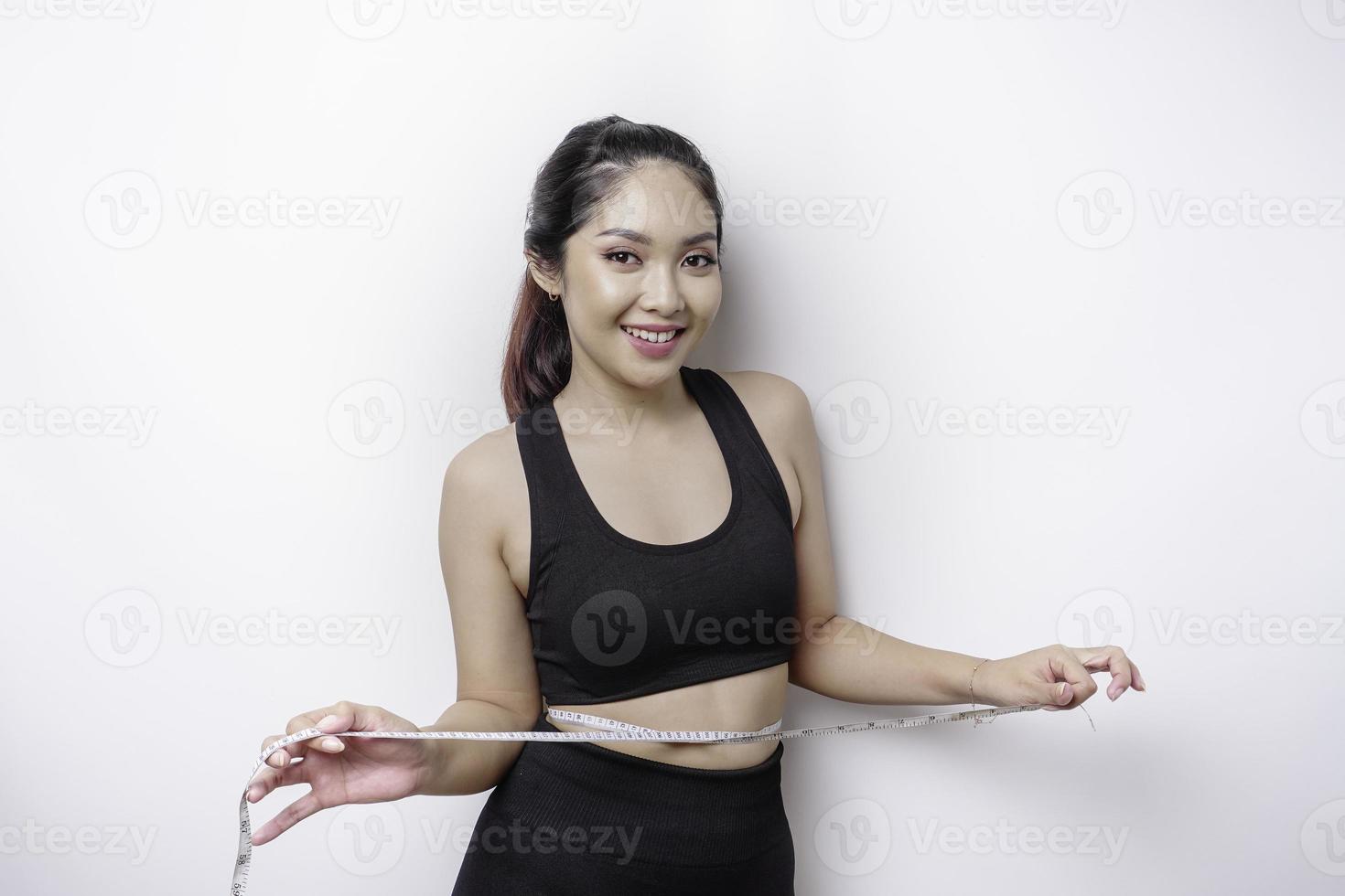 retrato de uma jovem asiática alegre em roupas esportivas, medindo a cintura com fita adesiva, sentindo-se feliz por perder peso em casa. estilo de vida saudável, esportes e conceito de dieta de emagrecimento foto