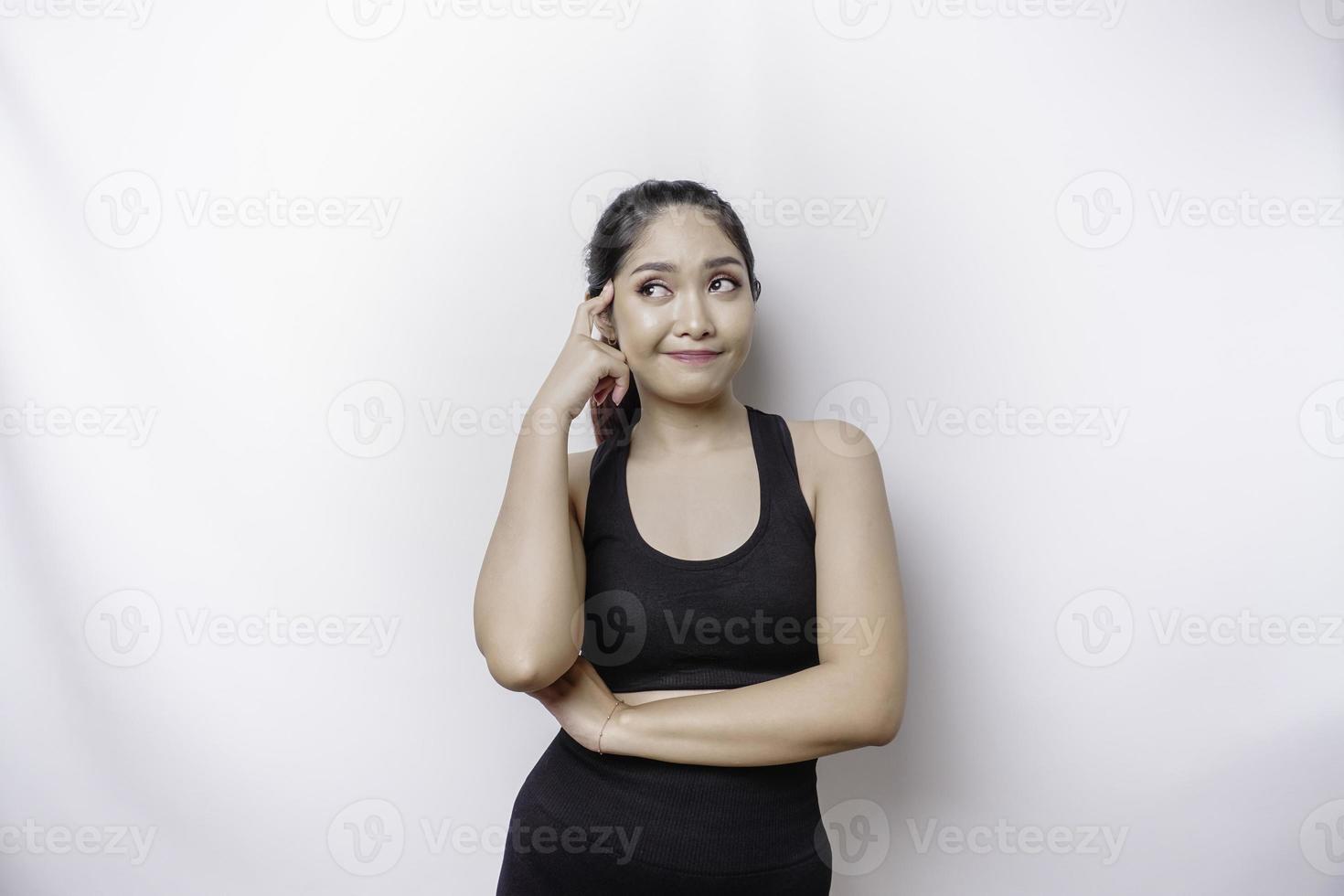 mulher asiática esportiva pensativa vestindo roupas esportivas está olhando de lado enquanto toca o queixo, isolado por fundo branco. foto