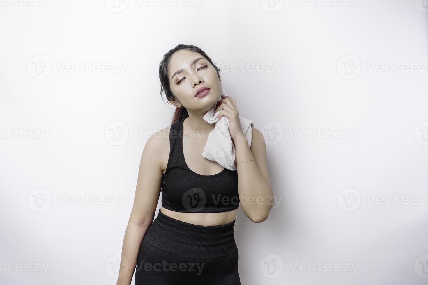 mulher asiática esportiva posando com uma toalha no ombro, cansada após o treino foto