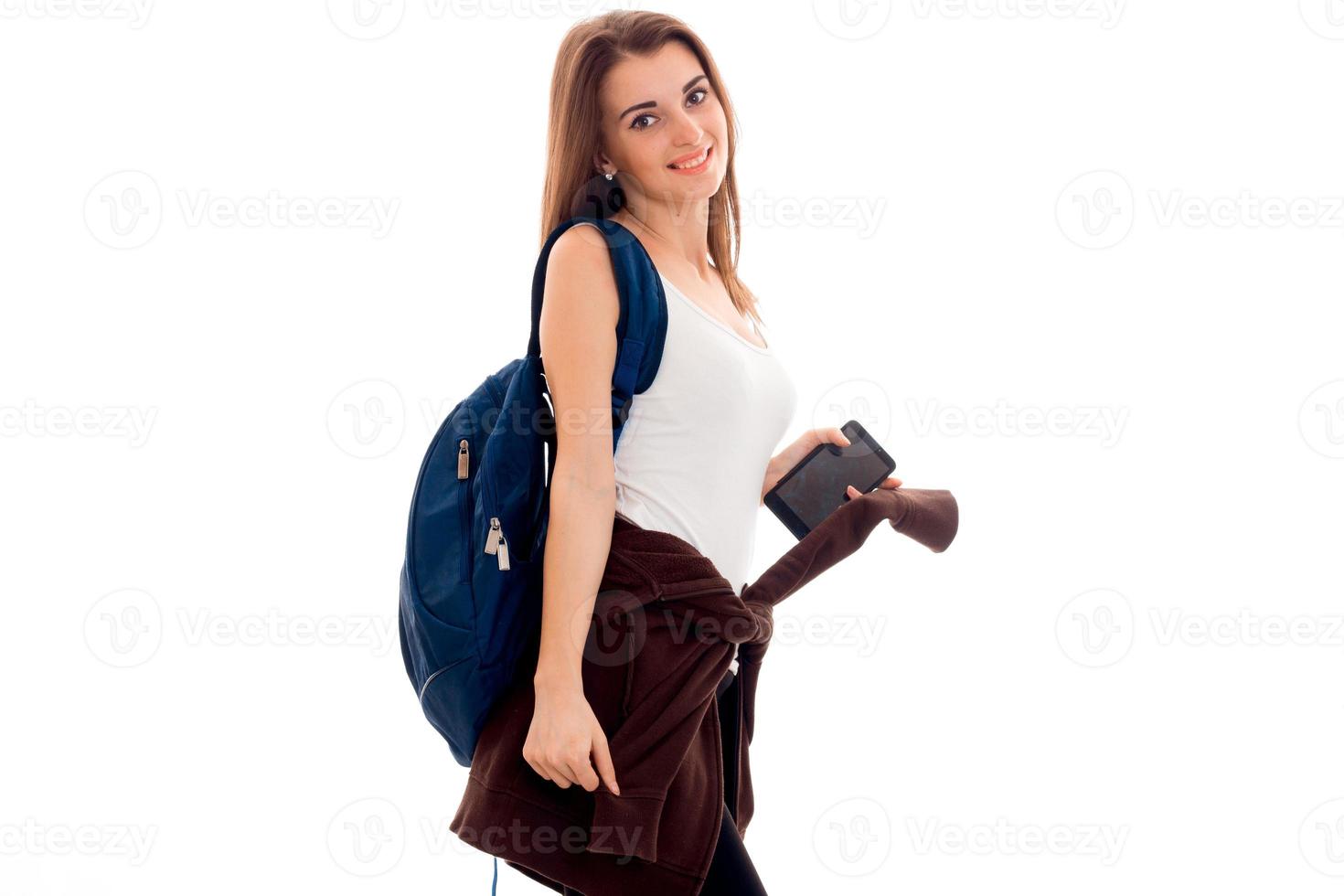 jovem estudante morena com mochila azul e telefone celular nas mãos dela posando e olhando para a câmera isolada no fundo branco foto