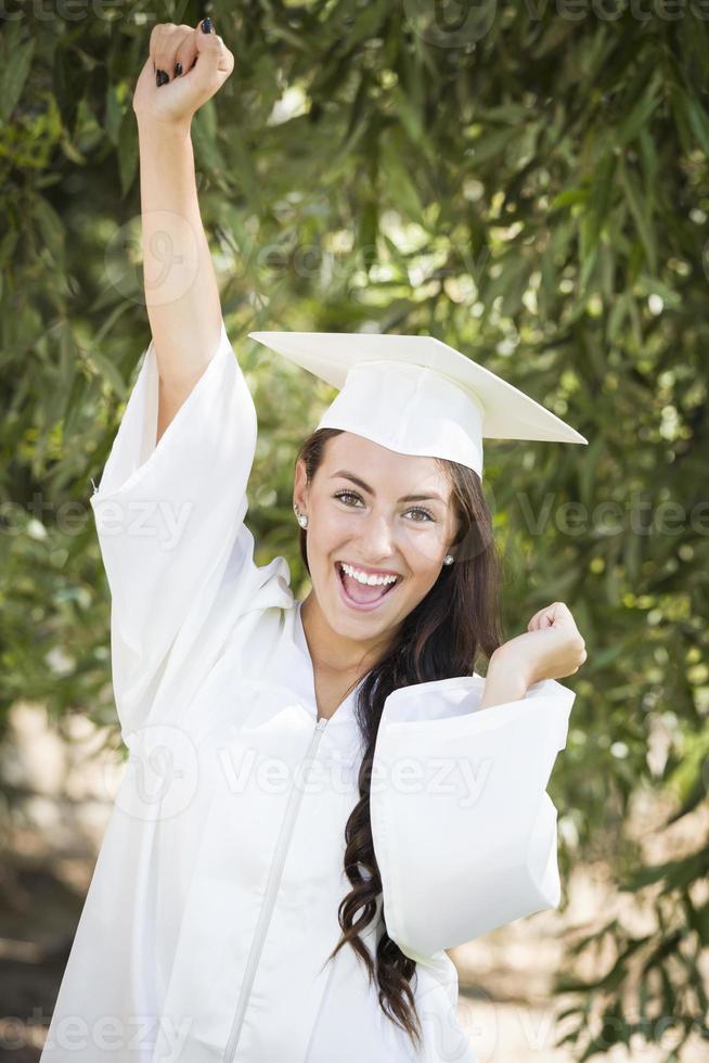 feliz graduando-se menina de raça mista em boné e vestido foto