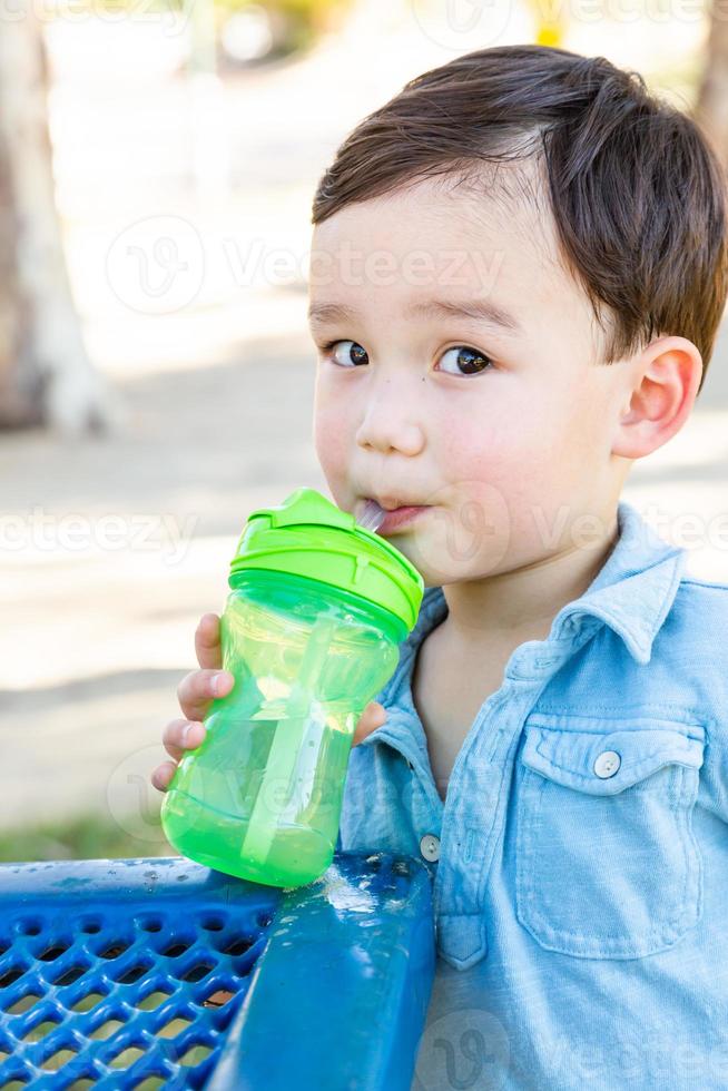 menino chinês e caucasiano bebendo água no playground. foto