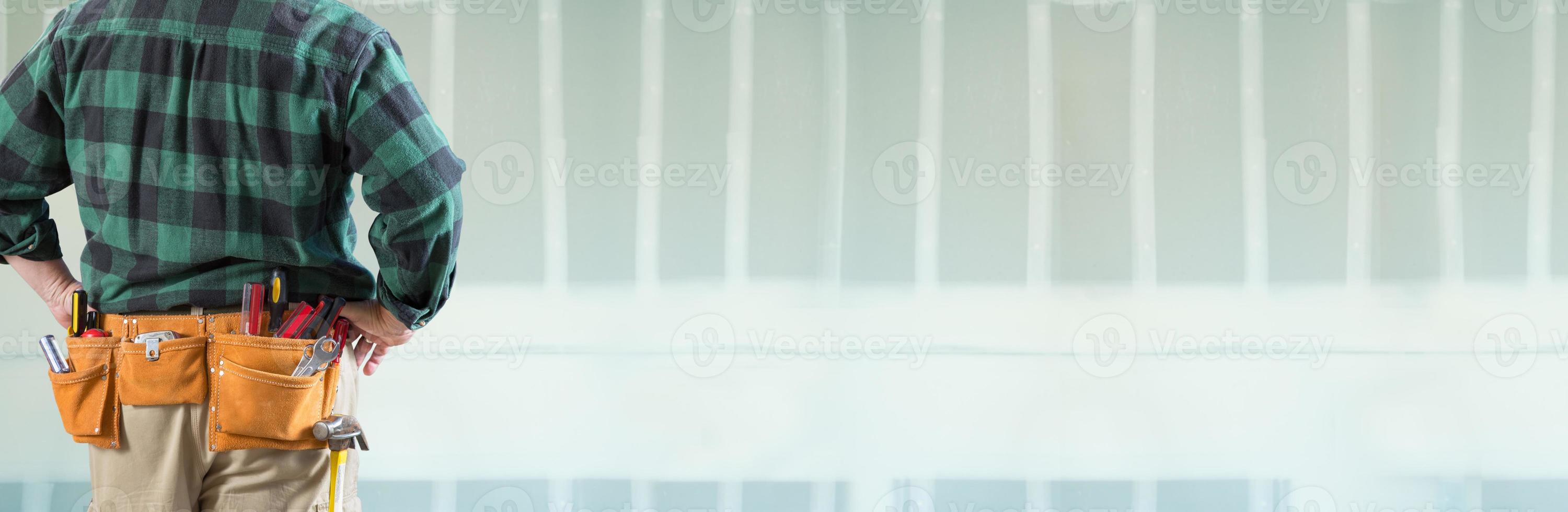 empreiteiro masculino usando cinto de ferramentas voltado para banner de drywall em branco foto