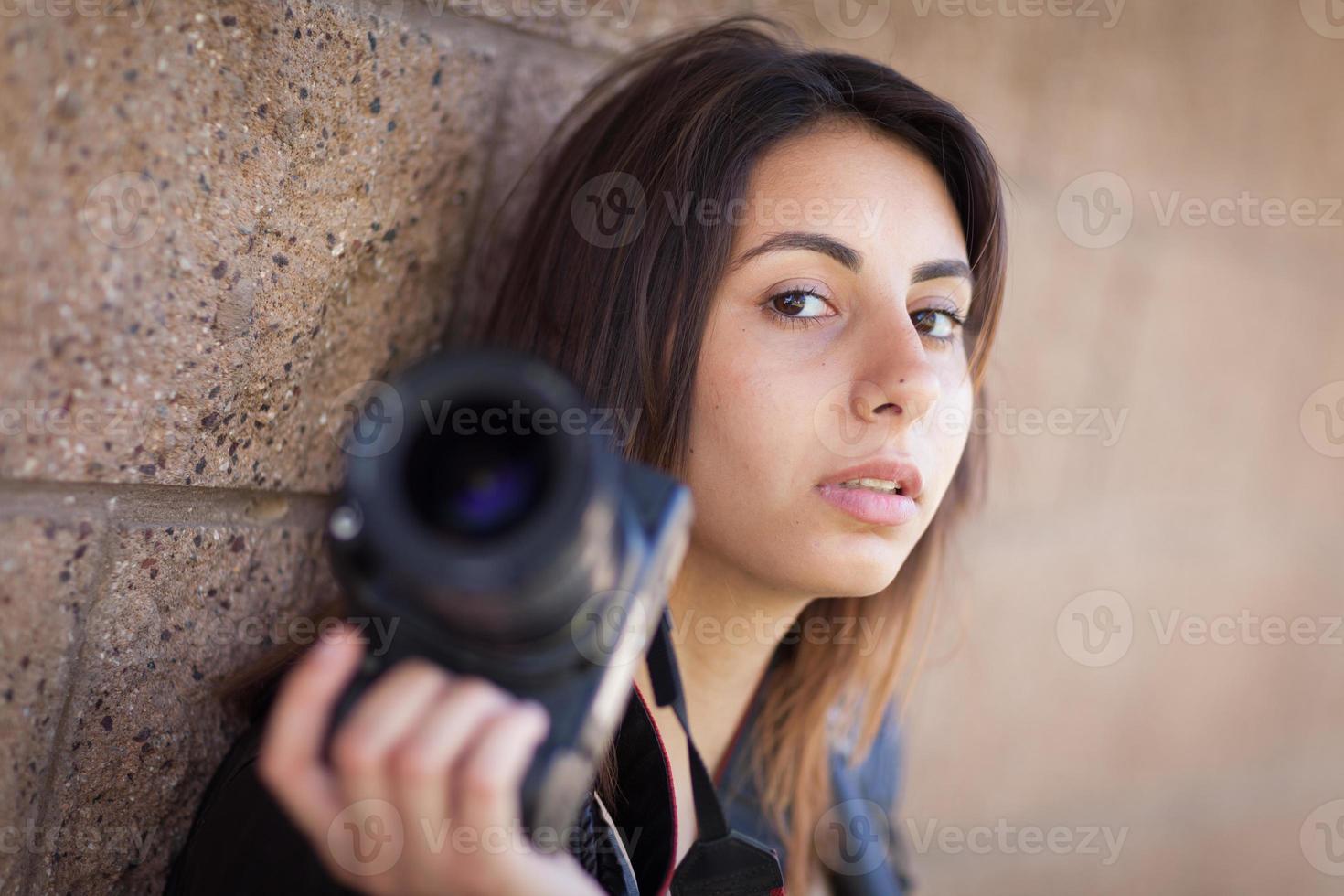 jovem fotógrafo feminino étnico adulto contra a parede segurando a câmera. foto