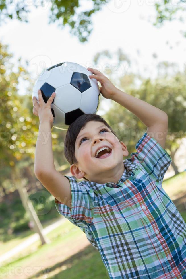 menino bonitinho brincando com bola de futebol ao ar livre no parque. foto