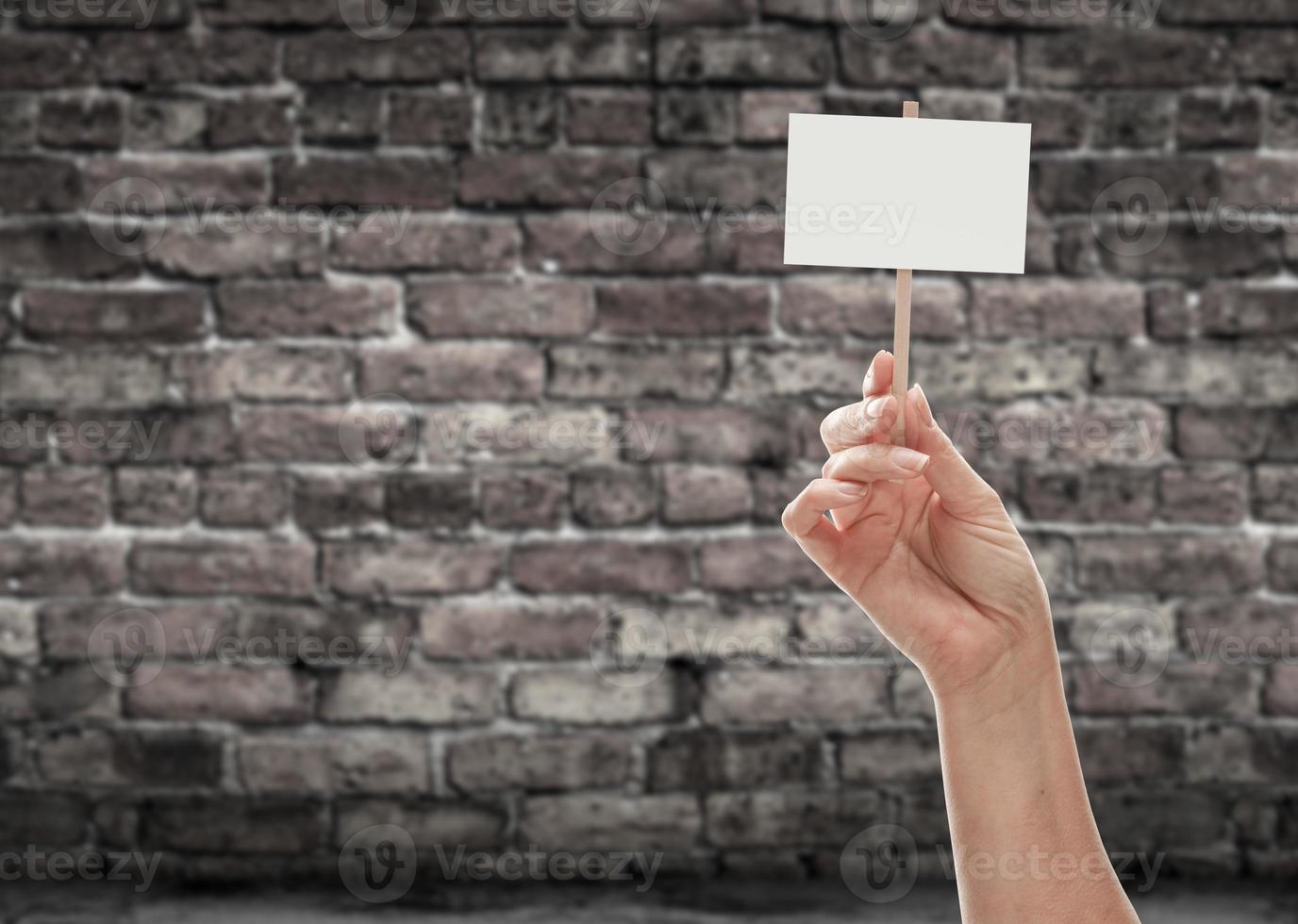 mão feminina segurando placa em branco contra a parede de tijolos envelhecidos foto