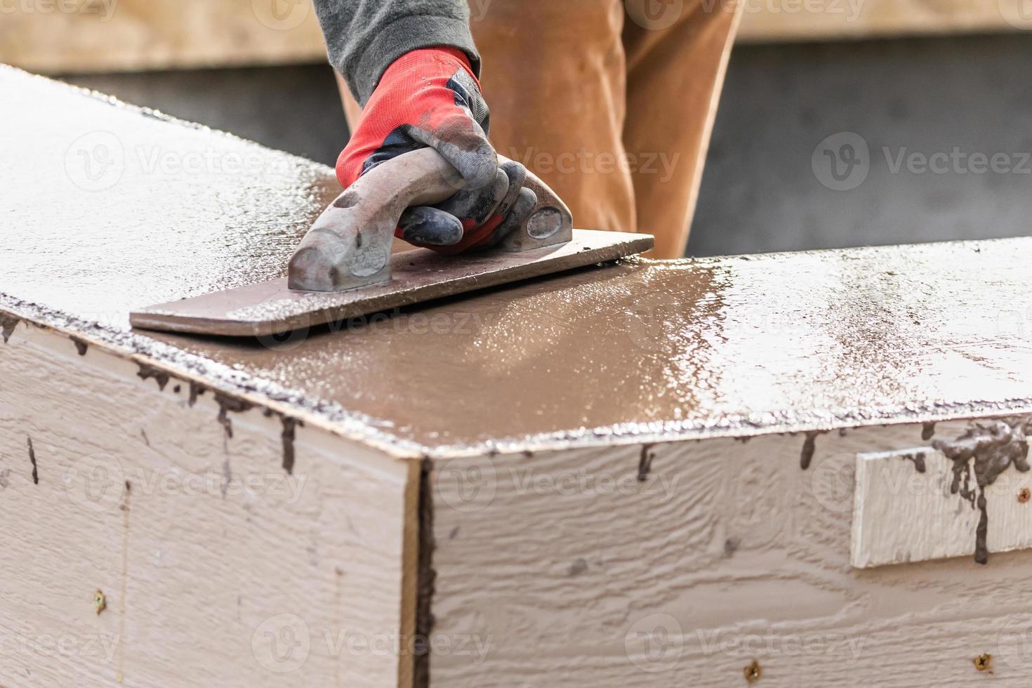 trabalhador da construção civil usando espátula de madeira em cimento úmido formando coping ao redor da nova piscina foto