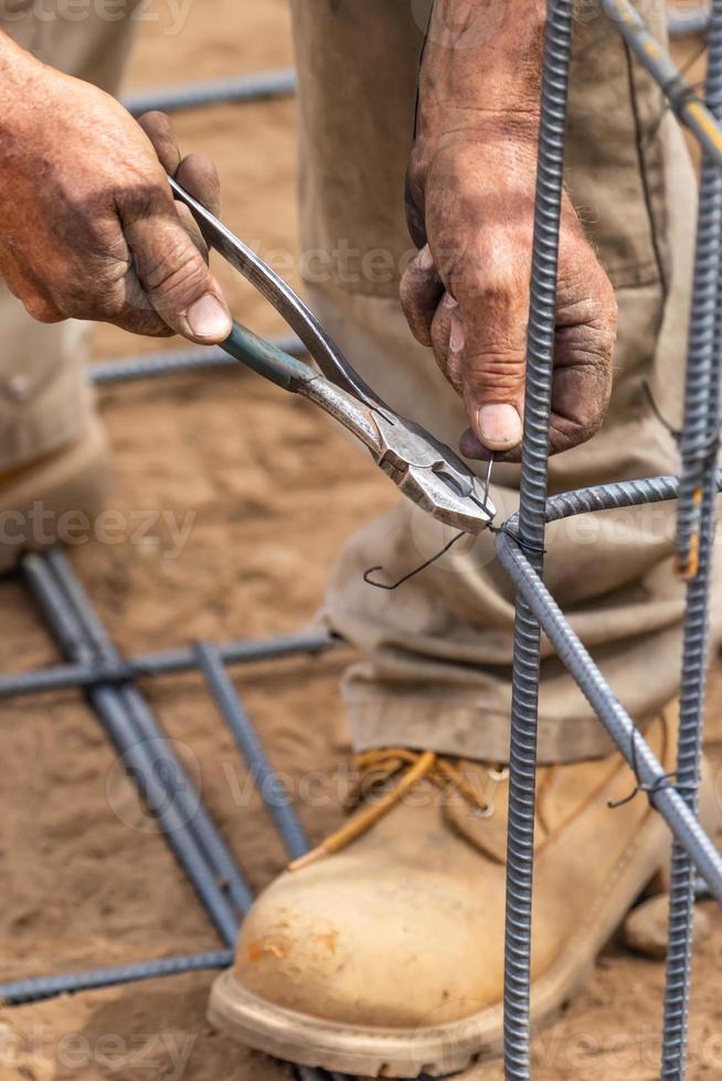 trabalhador protegendo armação de vergalhões de aço com ferramenta de corte de alicate de arame no canteiro de obras foto