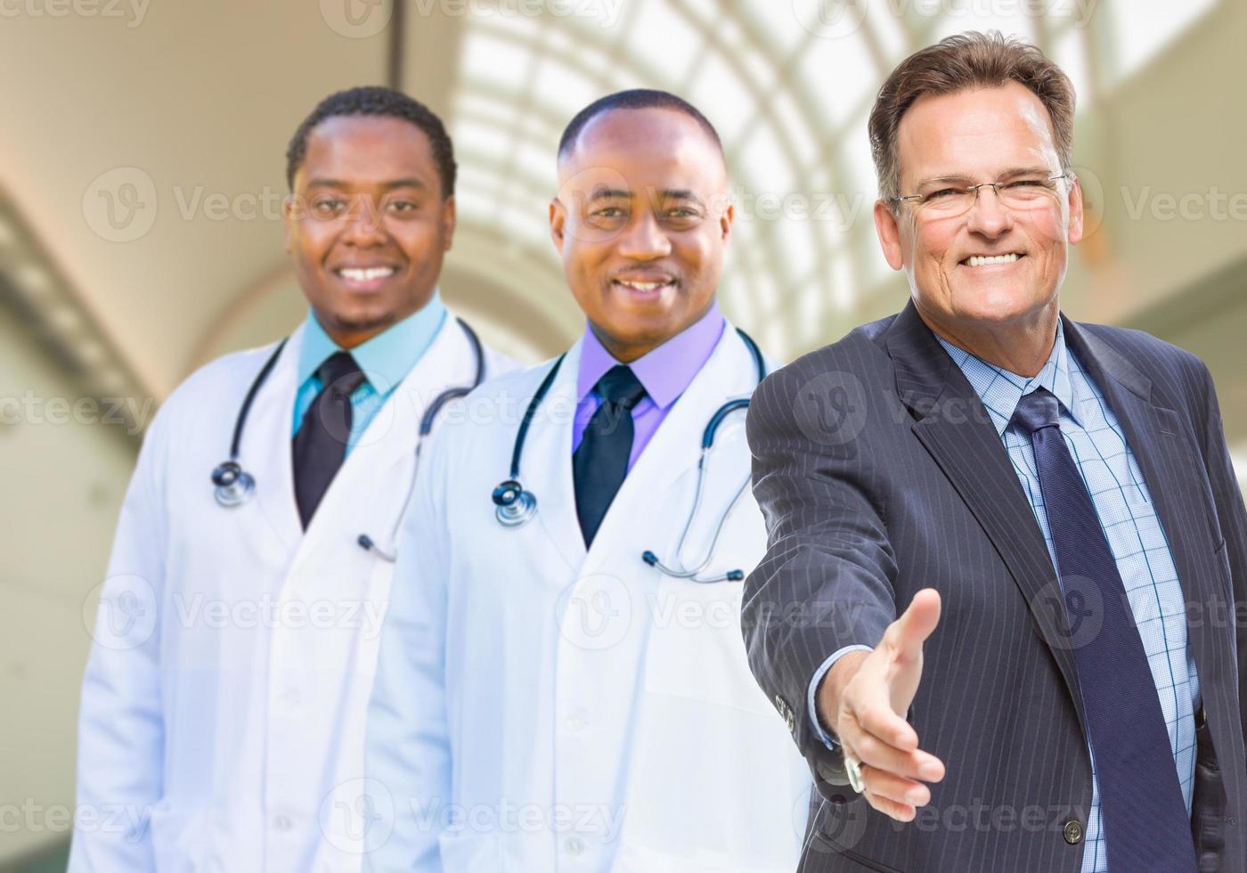 médicos de raça mista atrás de empresário alcançando aperto de mão dentro do hospital foto