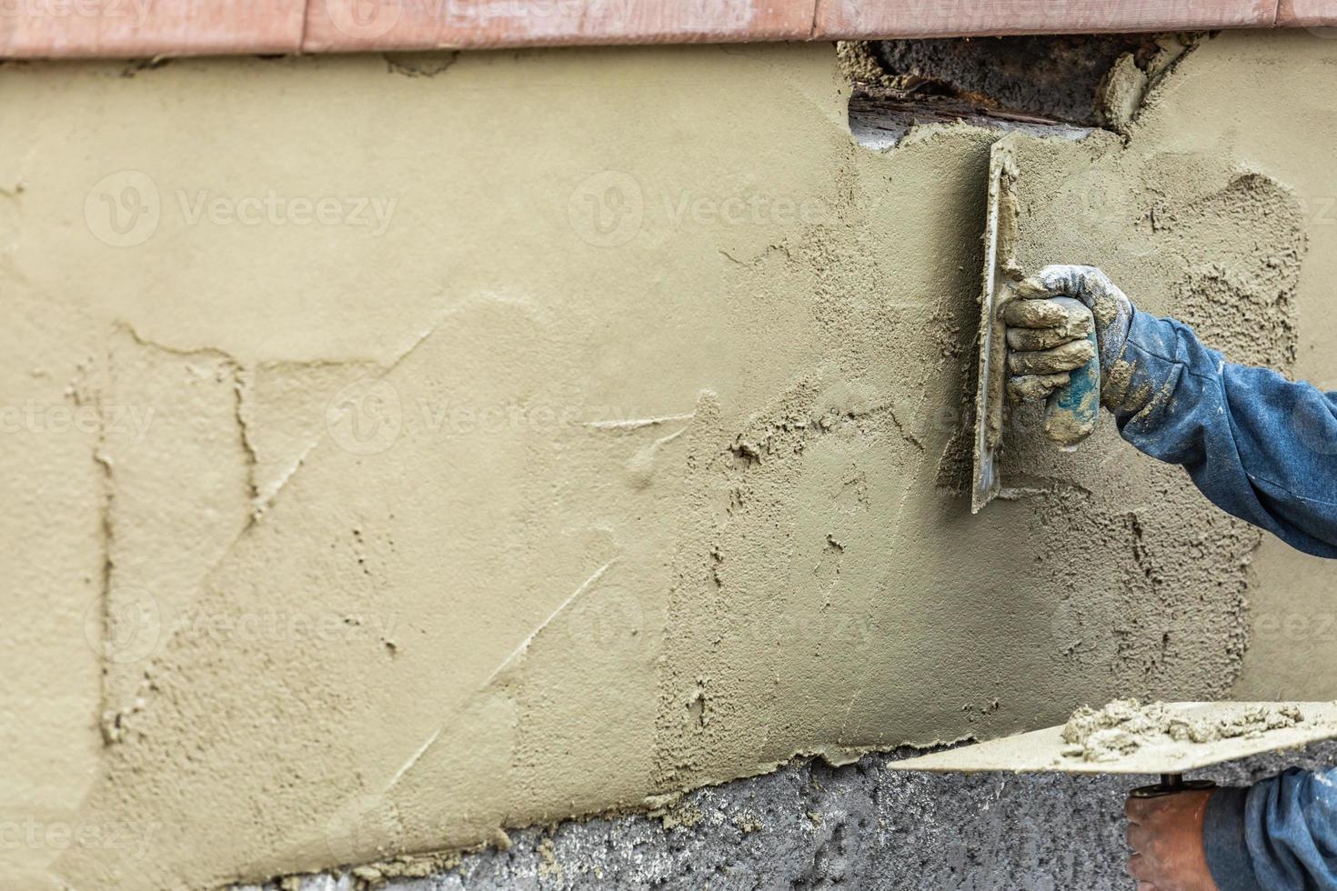 trabalhador de azulejo aplicando cimento com espátula no canteiro de obras da piscina foto