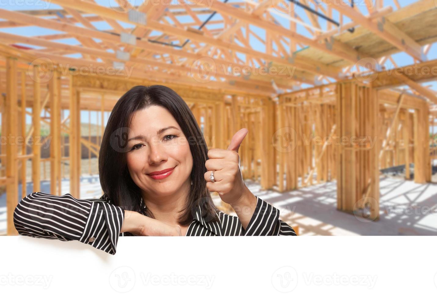 mulher hispânica com polegares para cima no local dentro do novo enquadramento de construção de casa. foto