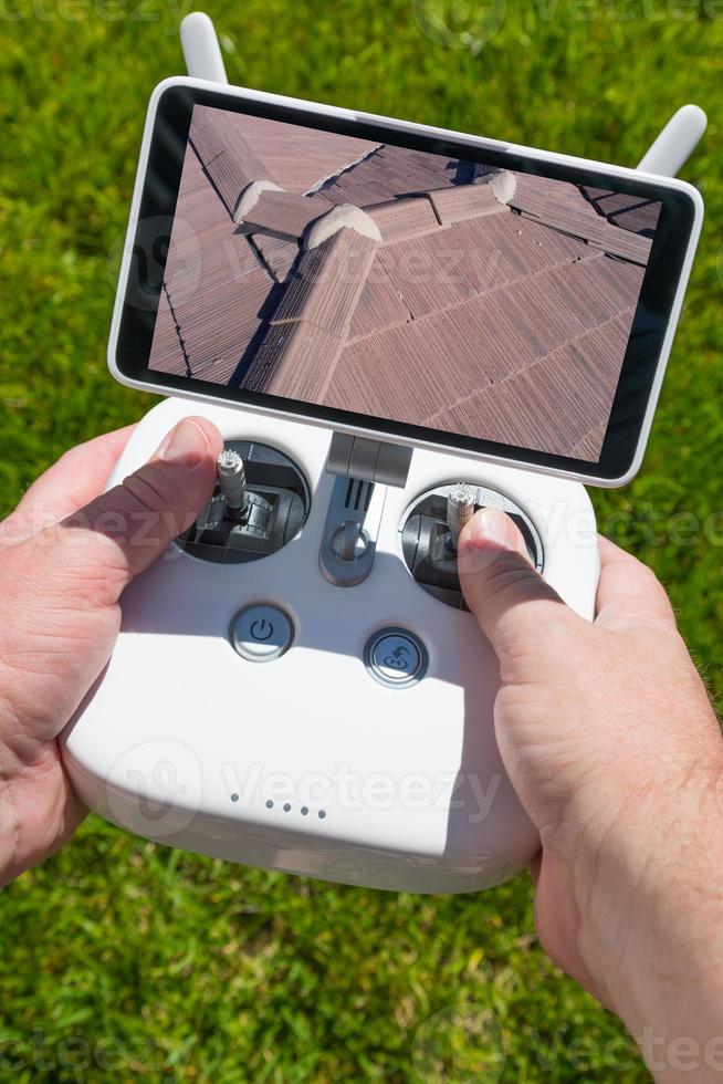 mãos segurando o controlador de drone quadcopter com imagem de telhado residencial na tela foto