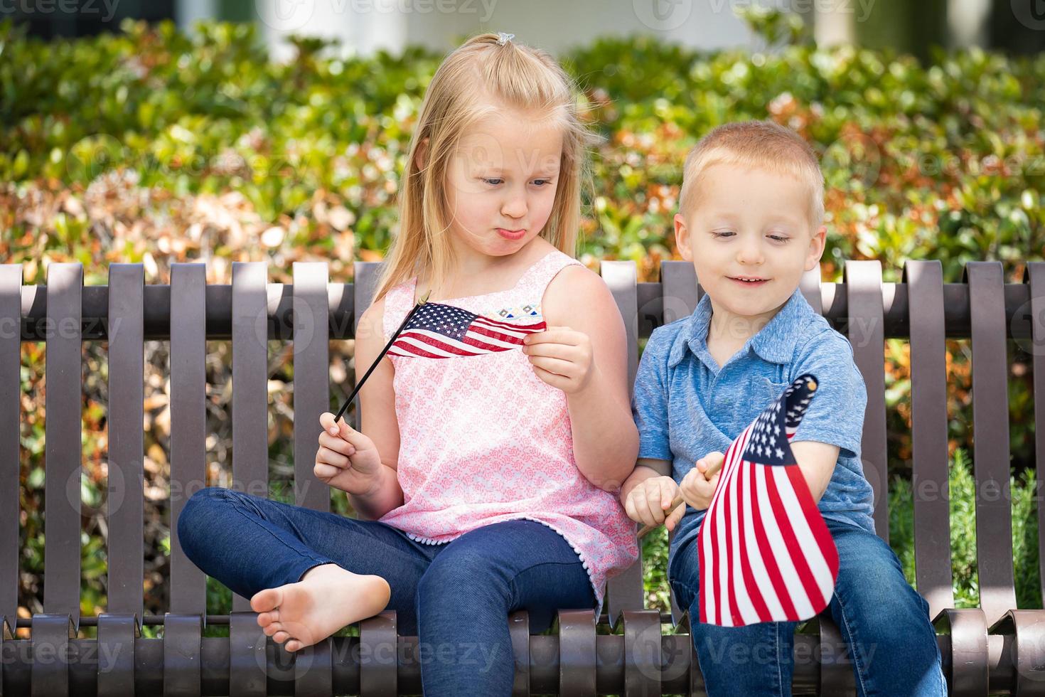 jovem irmã e irmão comparando o tamanho da bandeira americana no banco do parque foto