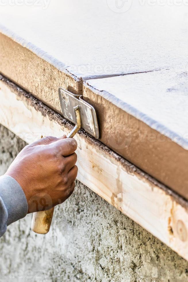 trabalhador da construção civil usando sulcador de mão em cimento úmido formando coping em torno de uma nova piscina foto