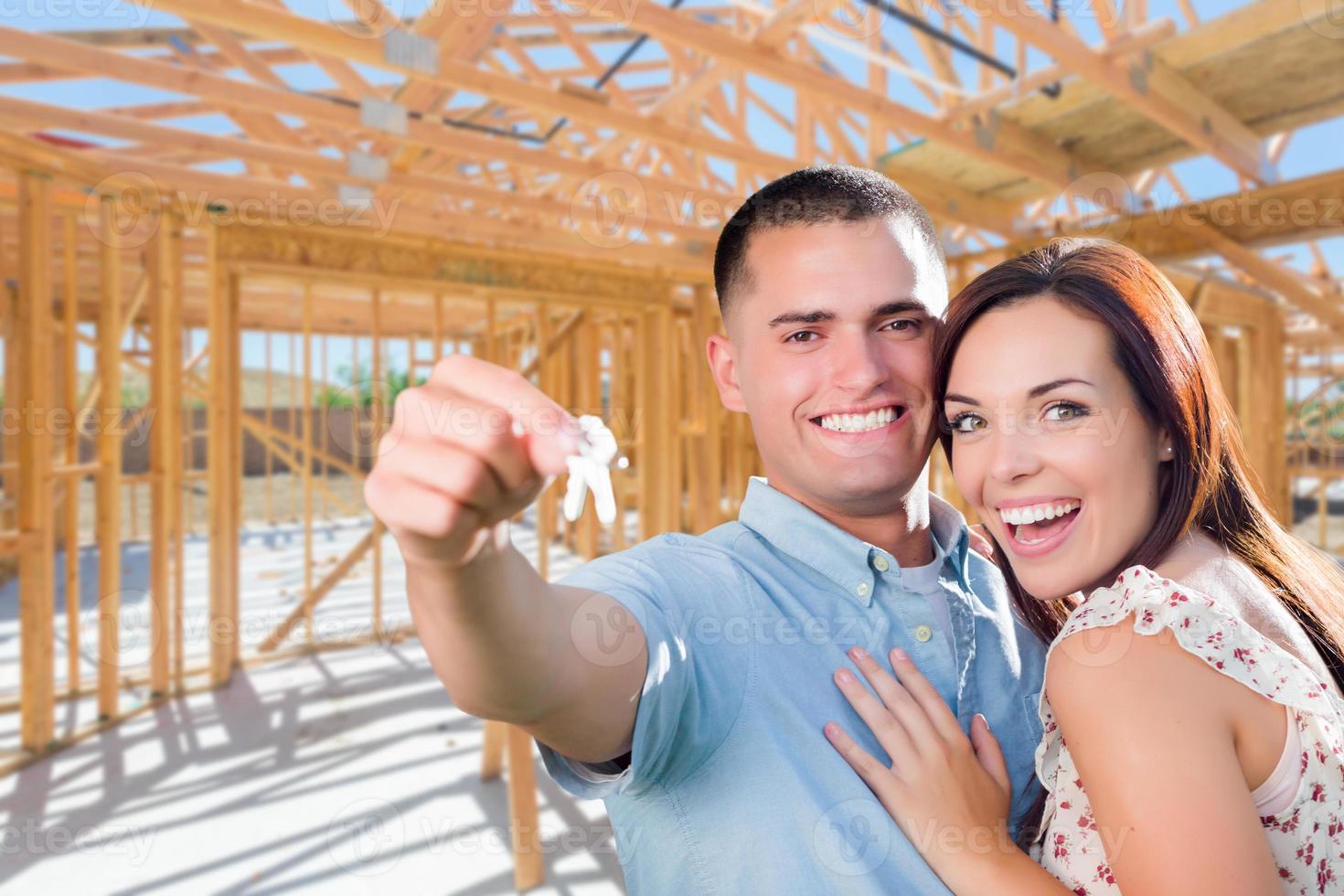 jovem casal militar no local com as chaves da casa dentro de sua nova estrutura de construção de casa. foto