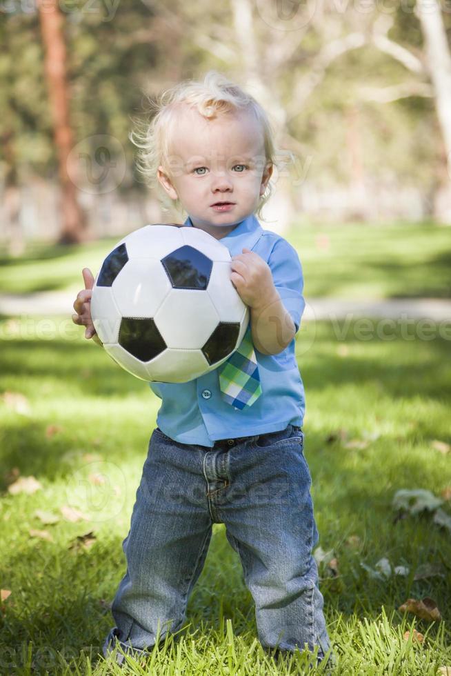 menino bonito brincando com bola de futebol no parque foto