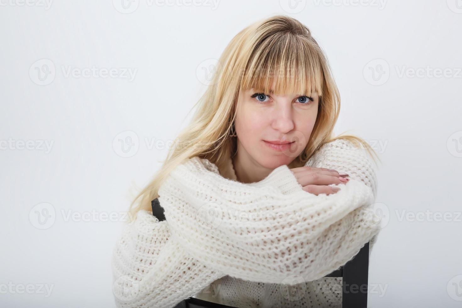 feche o retrato do modelo de menina loira em suéter de lã branca sobre fundo branco no estúdio foto