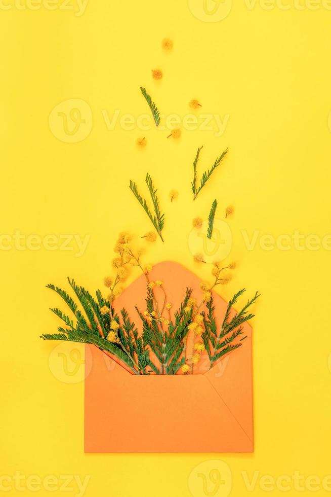 envelope laranja com ramos de mimosa e flores de mimosa e folhas voando em amarelo. foto