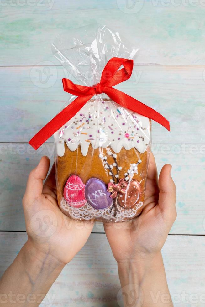 decoração de páscoa. mãos femininas segurando bolo de páscoa de gengibre embalado em celofane como presente em pano de fundo de madeira. foto