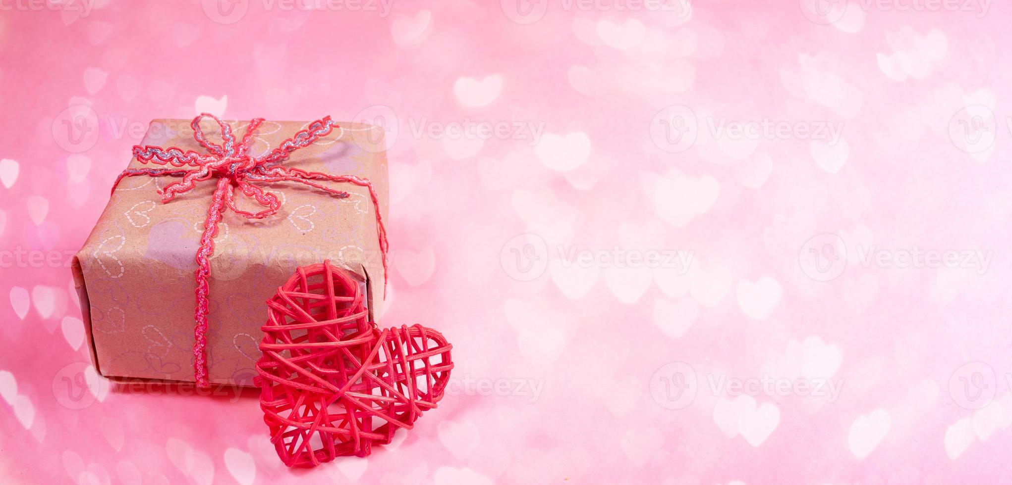 bandeira rosa festiva do dia dos namorados com caixa de presente embrulhada diy e coração de vime vermelho no pano de fundo bokeh com corações. foto