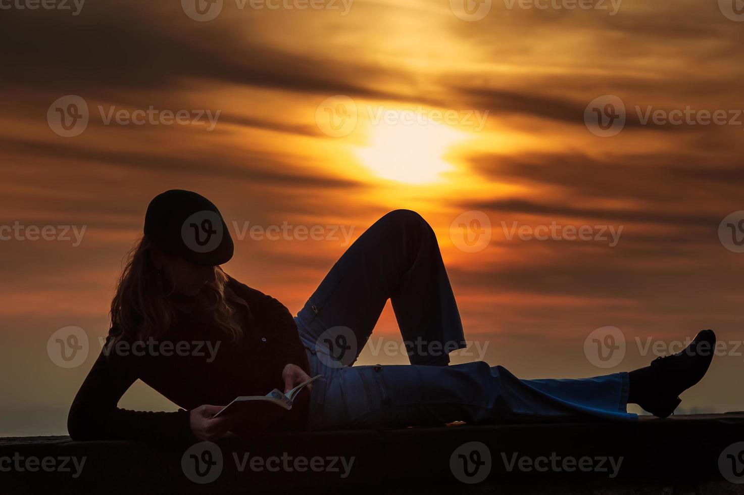 menina lendo um livro na parede ao pôr do sol foto