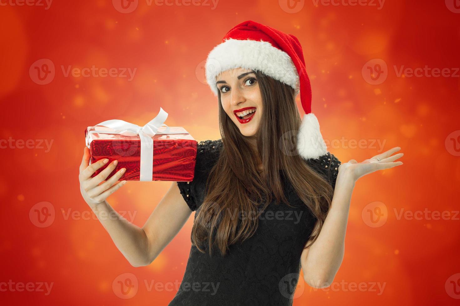 menina sorrindo com chapéu de Papai Noel com presente vermelho foto