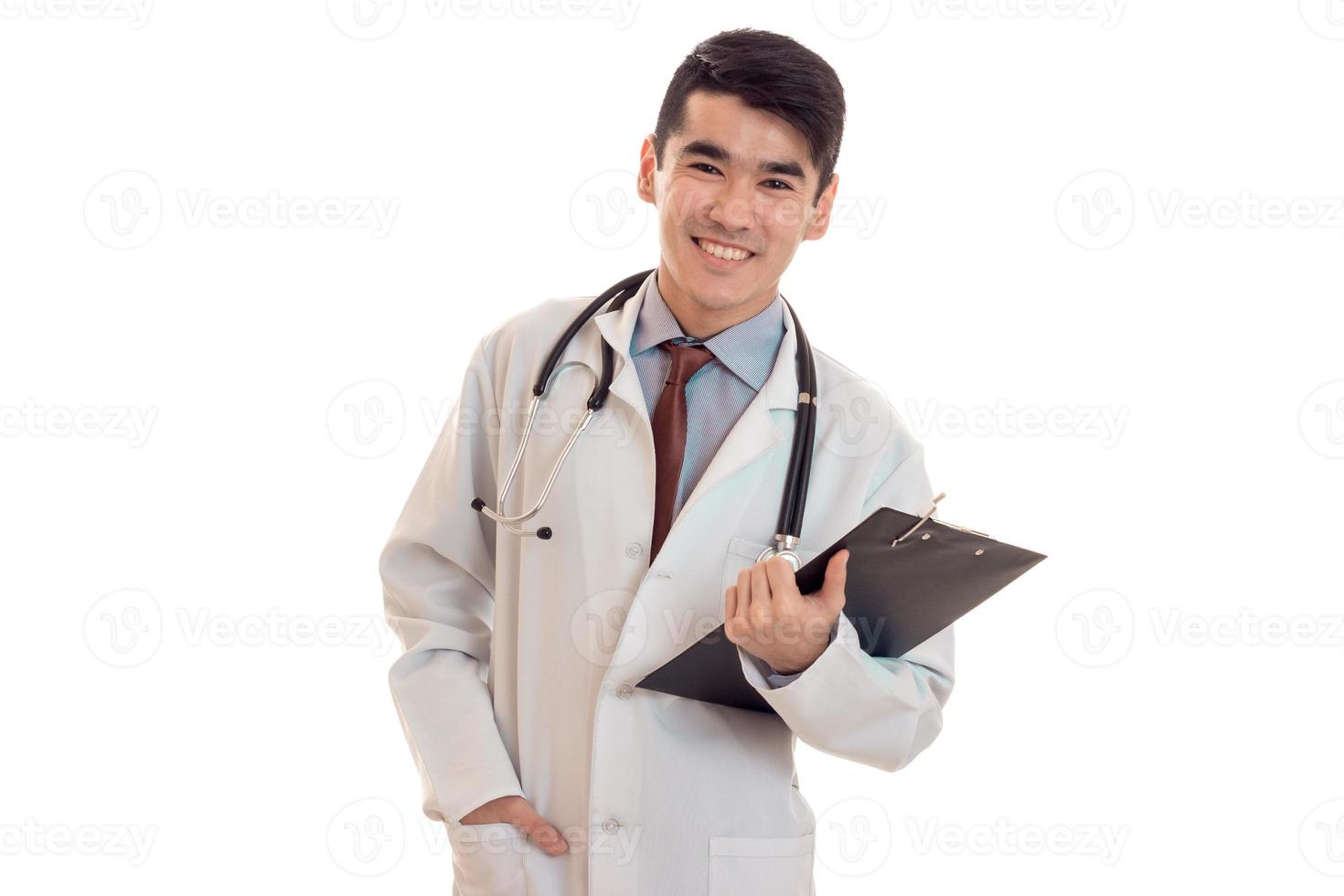 jovem morena feliz médico de uniforme com estetoscópio nos ombros faz anotações isoladas no fundo branco foto
