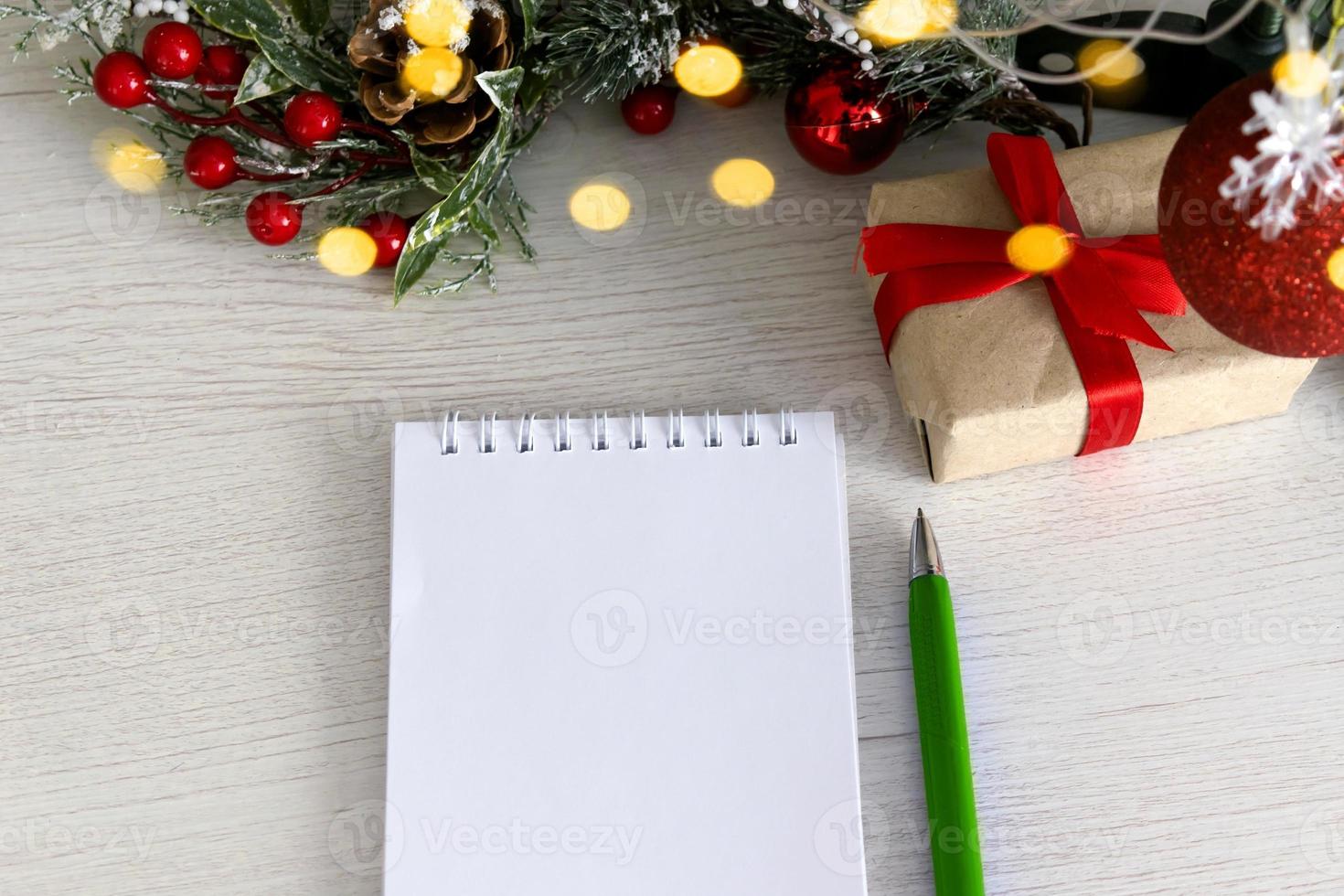 bloco de notas com caneta em fundo de madeira com decoração e luz de presente e natal foto