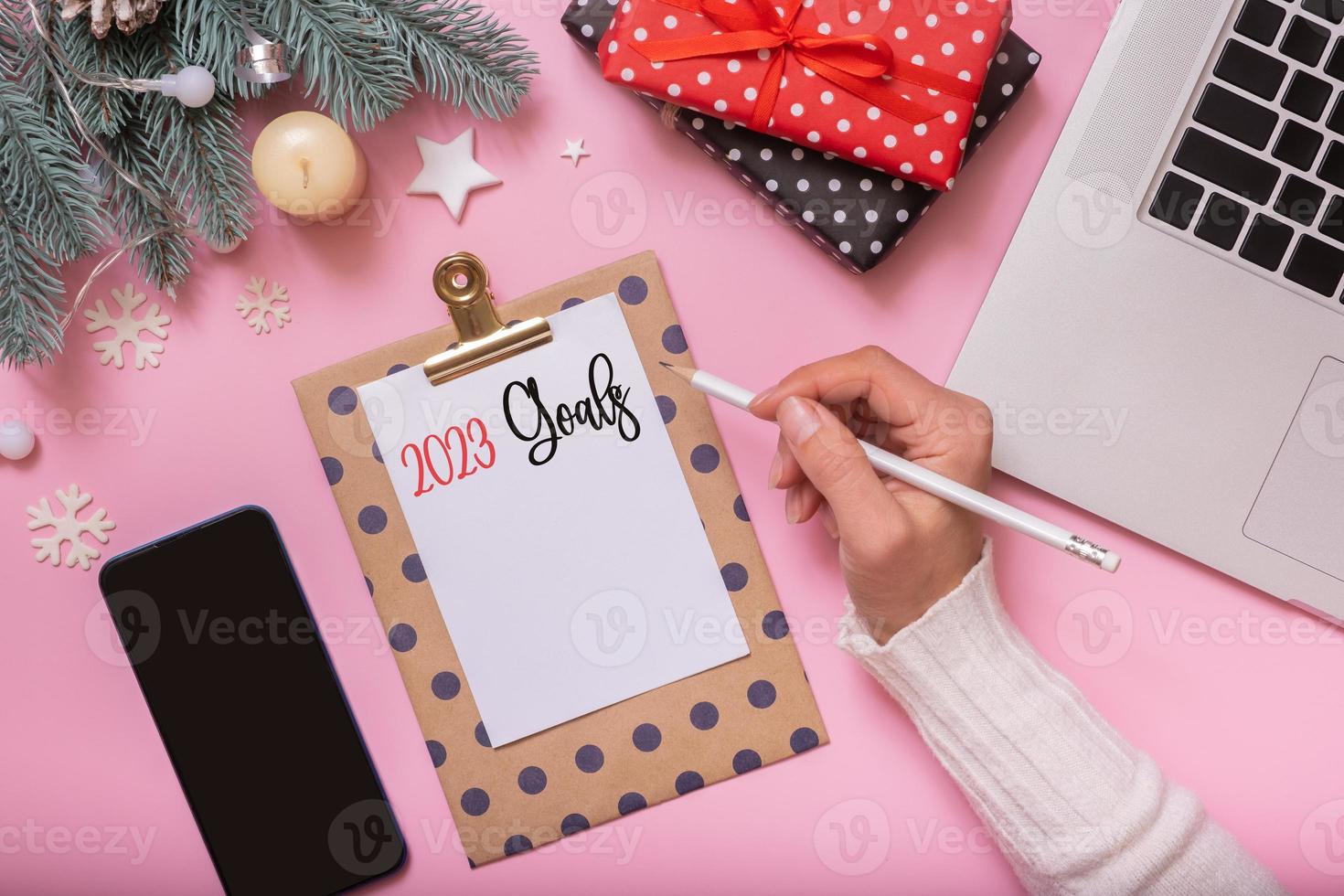 2023 metas escritas à mão feminina e decoração de mesa de trabalho de ano novo de natal vista superior, configuração plana em fundo rosa foto