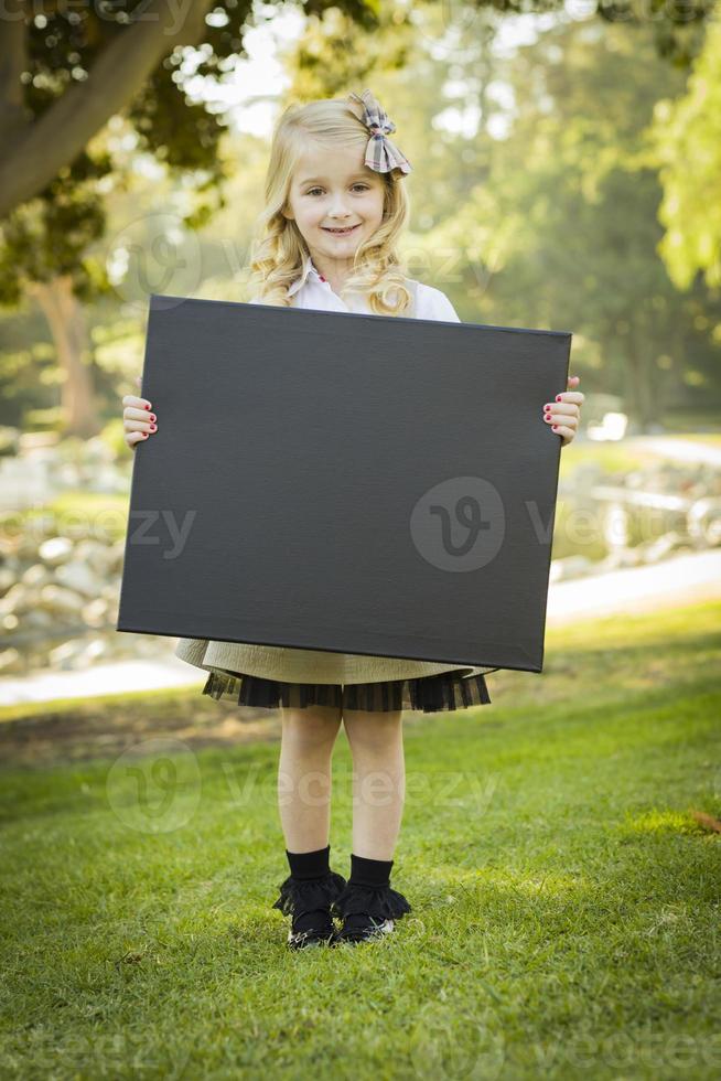 linda garotinha loira segurando uma lousa preta ao ar livre foto