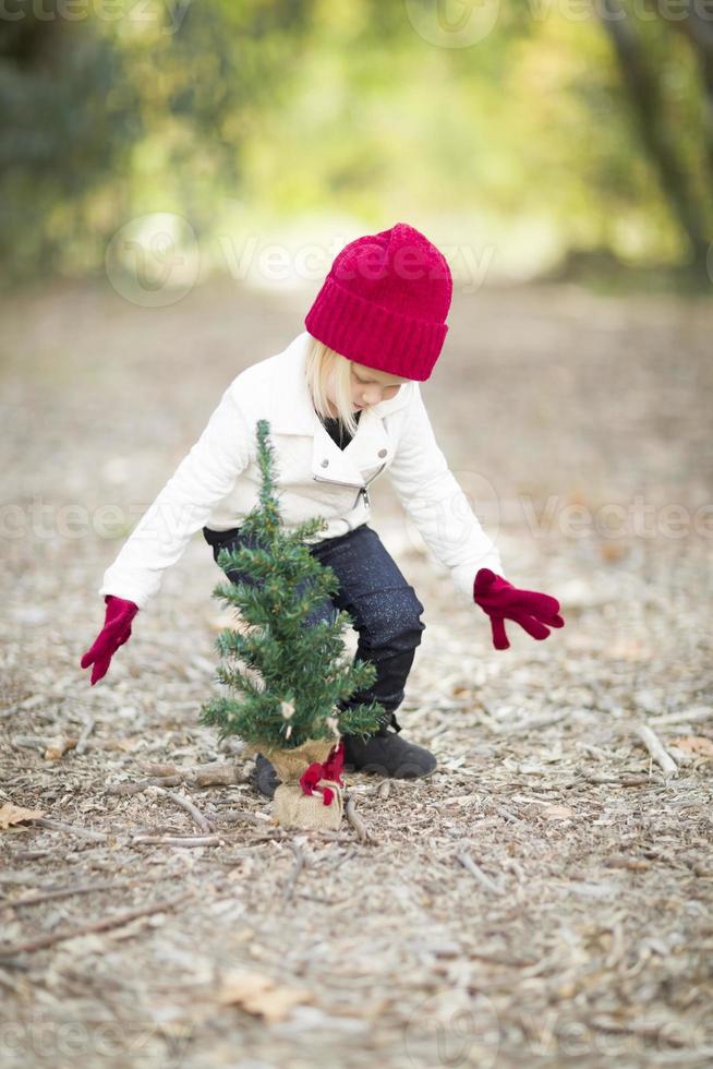 garota de luvas vermelhas e boné perto de pequena árvore de Natal foto