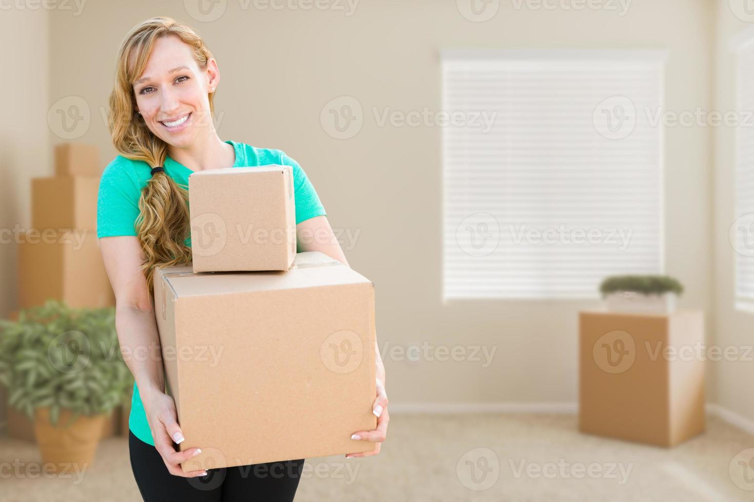 adulta jovem feliz segurando caixas em movimento no quarto vazio em uma casa nova. foto