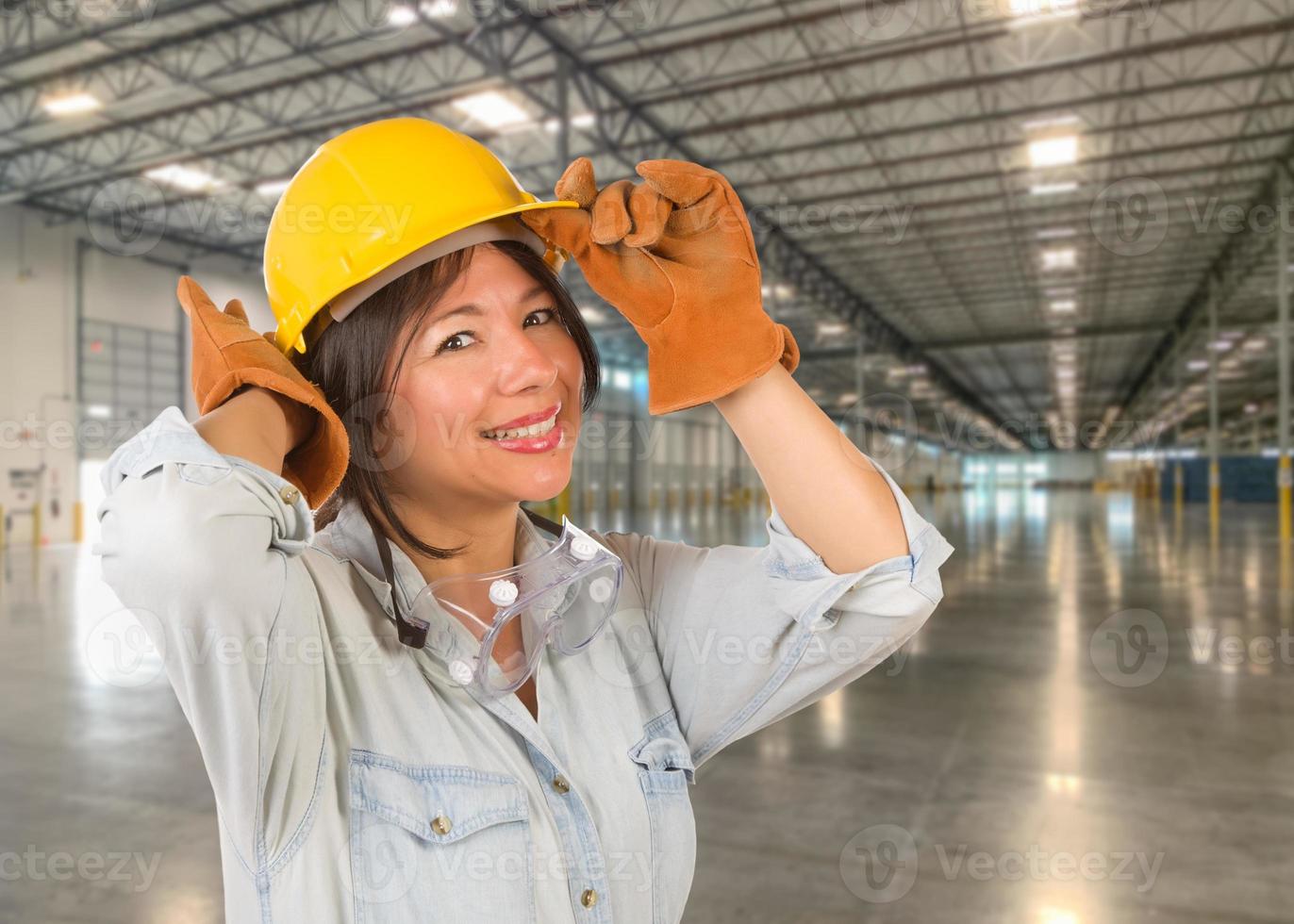 empreiteiro feminino hispânico usando capacete em pé no armazém industrial vazio. foto