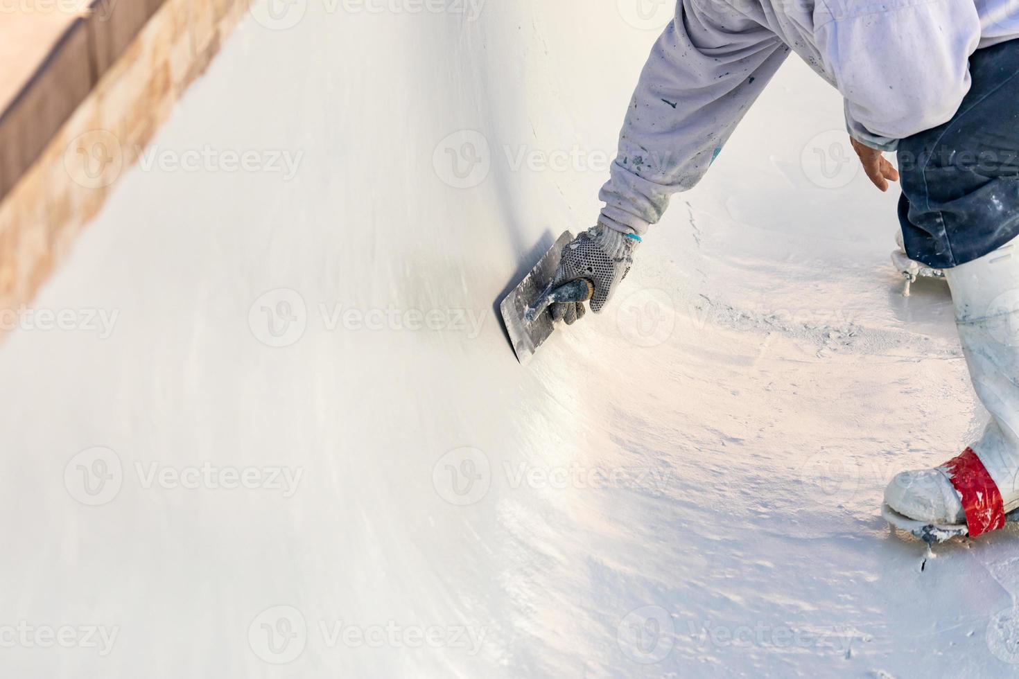 trabalhador usando sapatos pontiagudos alisando reboco de piscina molhada com espátula foto