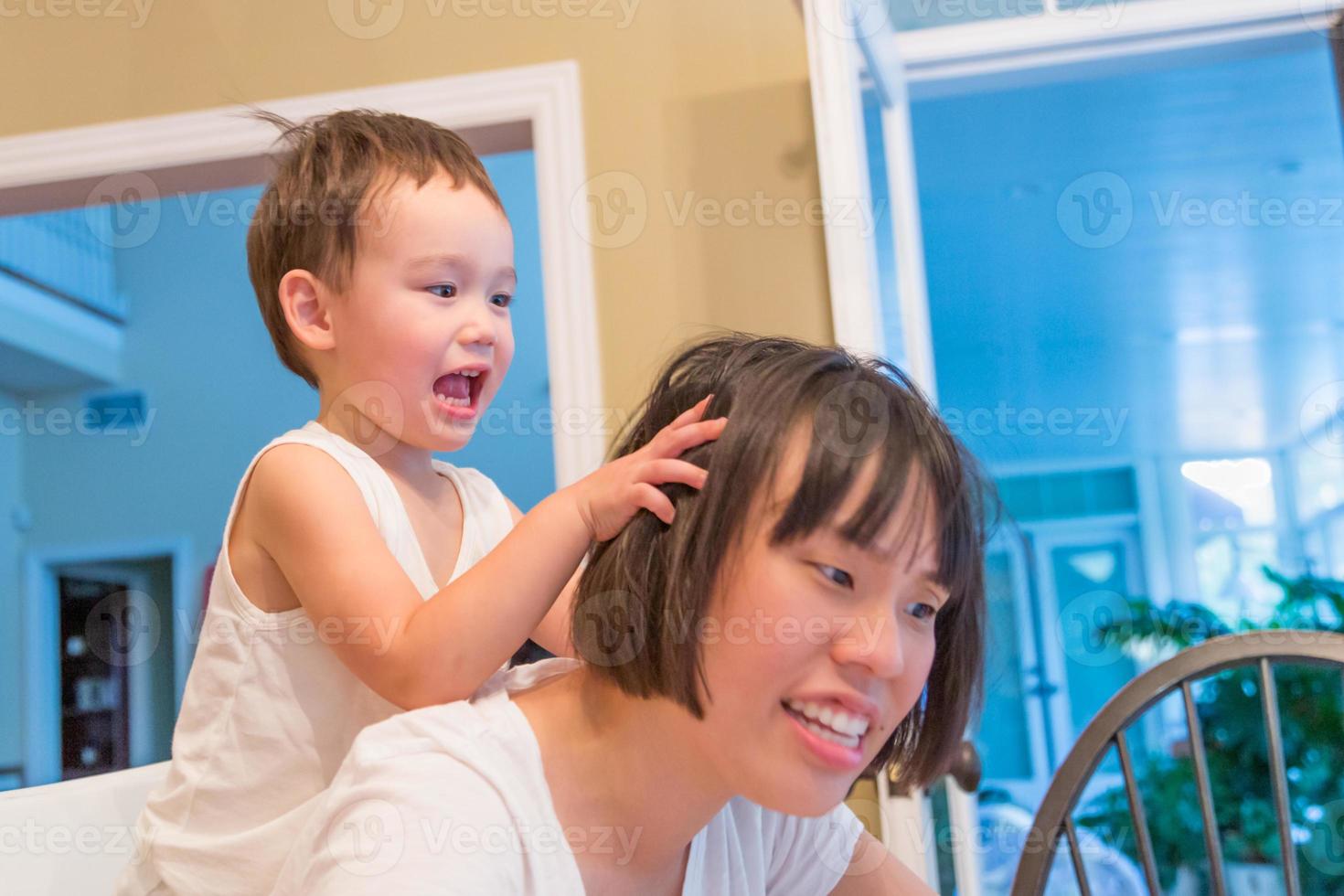 menino chinês e caucasiano de raça mista feliz se divertindo com a mãe chinesa dentro de casa foto