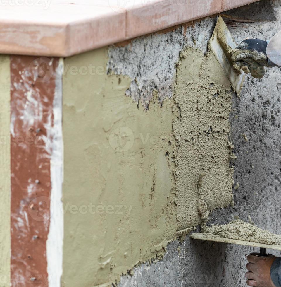 trabalhador de azulejo aplicando cimento com espátula no canteiro de obras da piscina foto