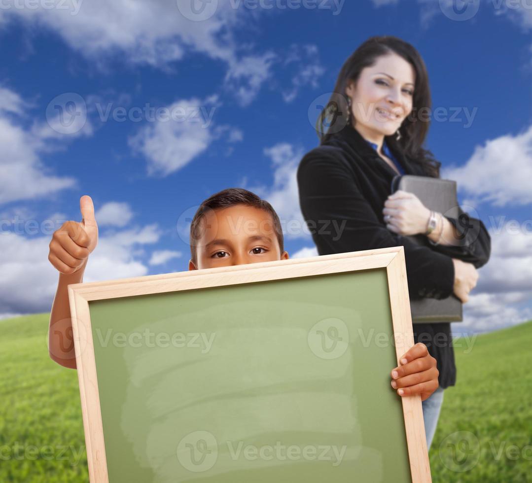 menino com quadro de giz em branco, professor atrás na grama foto