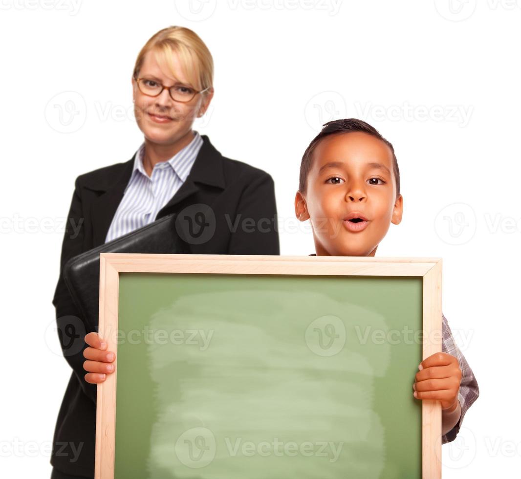 menino hispânico segurando quadro de giz e professora atrás foto