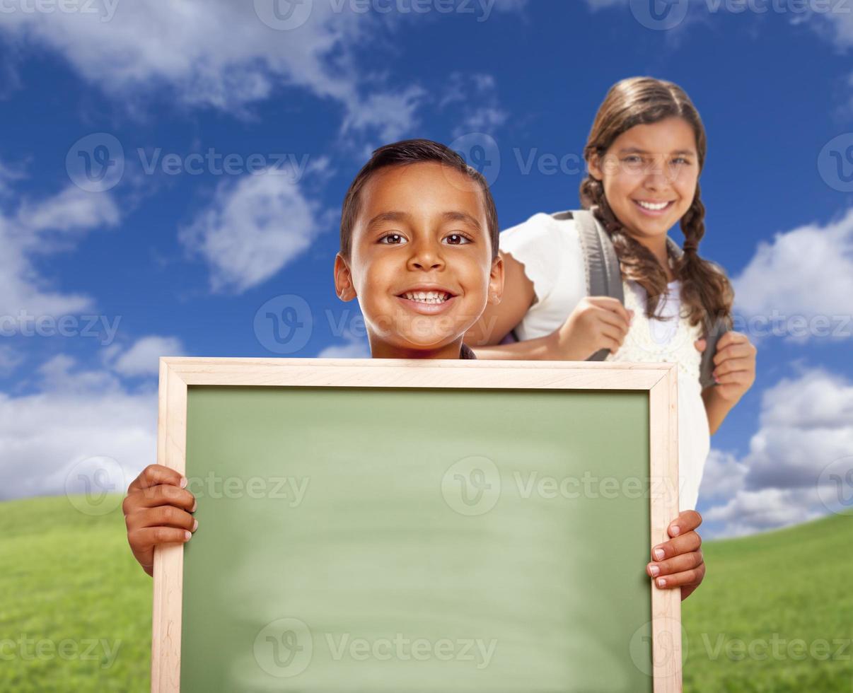 menino hispânico e menina no campo segurando o quadro de giz em branco foto