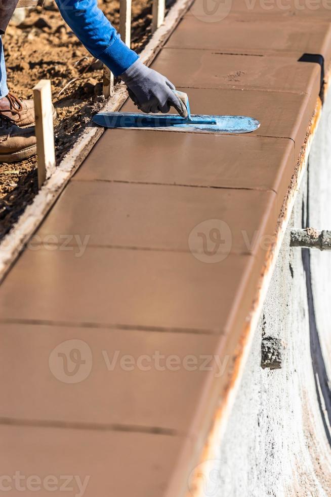 trabalhador da construção civil usando espátula em cimento molhado formando coping ao redor da nova piscina foto