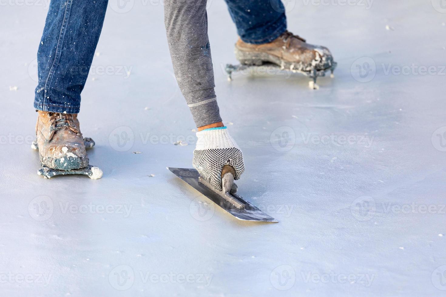 trabalhador usando sapatos pontiagudos alisando reboco de piscina molhada com espátula foto