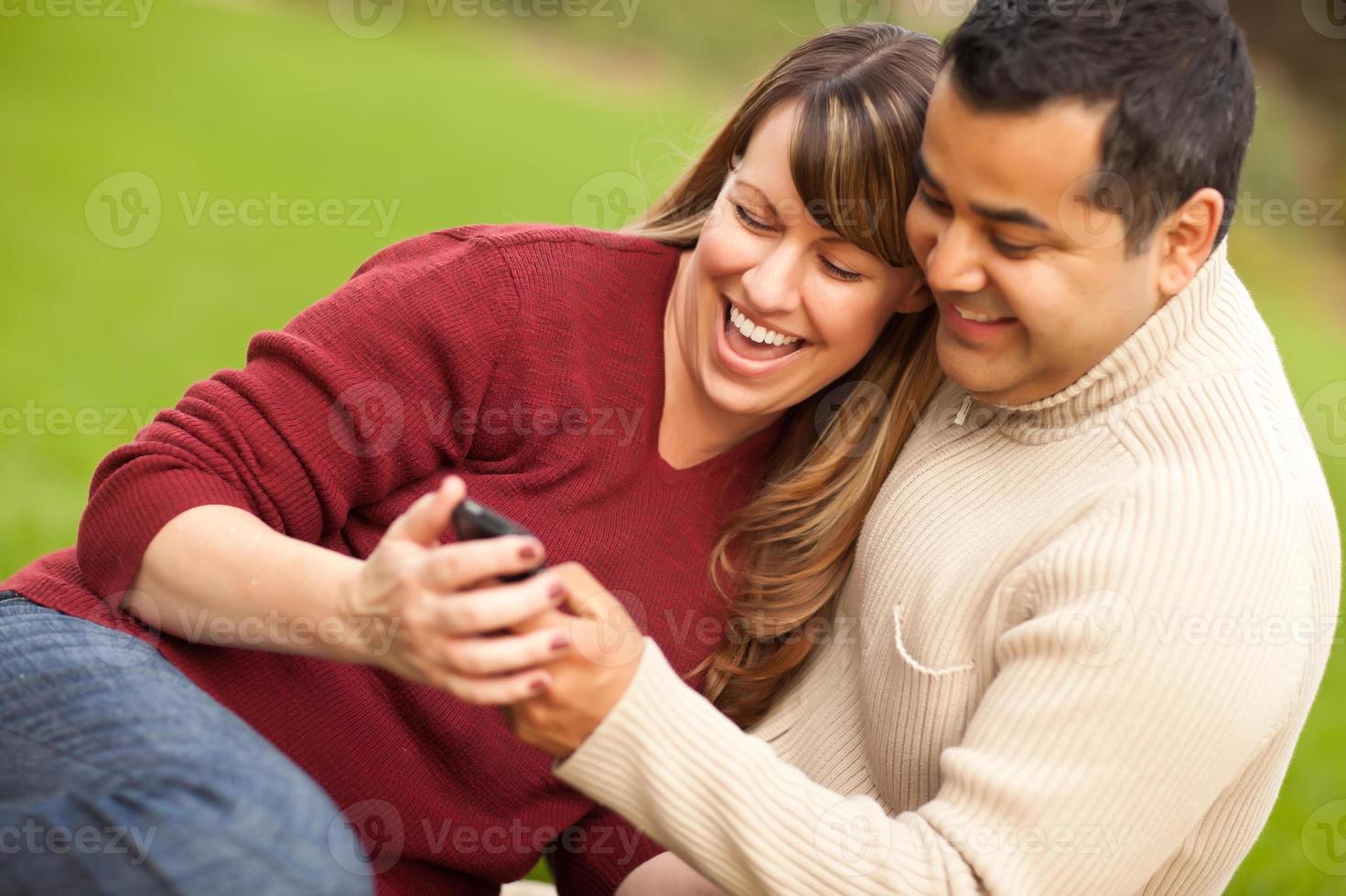 casal atraente de raça mista, desfrutando de seu telefone com câmera foto