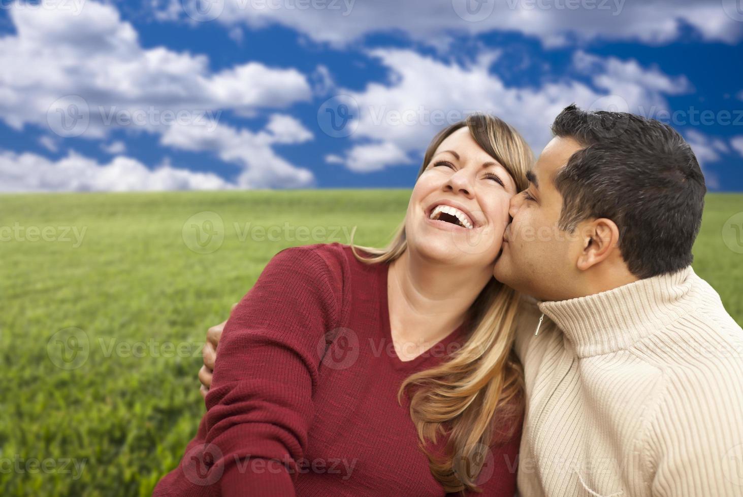 casal misto feliz sentado no campo de grama foto